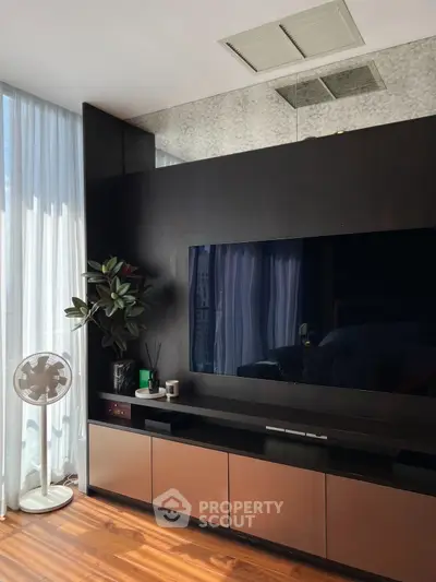 Modern living room with sleek entertainment unit and large TV, featuring elegant decor and natural light.