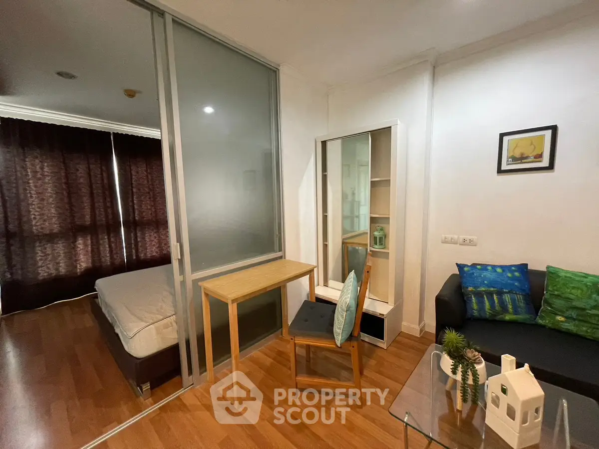 Cozy studio apartment with modern furnishings and wooden flooring, featuring a sliding glass partition and stylish decor.
