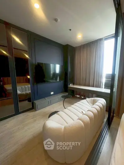 Modern living room with plush sofa and large TV, featuring floor-to-ceiling windows for natural light.