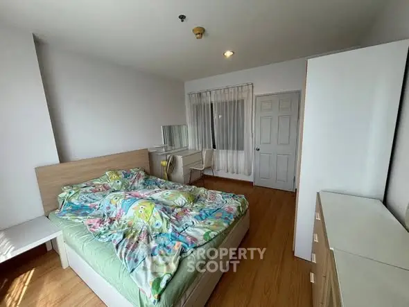 Spacious bedroom with wooden flooring and modern furniture in a bright apartment.