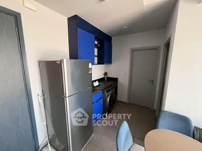 Modern compact kitchen with blue cabinets, stainless steel fridge, and washing machine in cozy apartment.