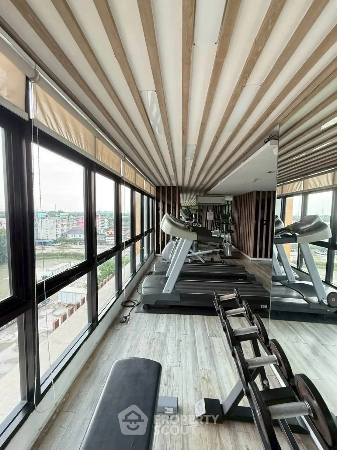 Modern gym with treadmills and weights in a high-rise building with panoramic city views.