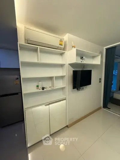 Modern apartment interior with sleek white shelving and mounted TV, featuring air conditioning and polished floors.