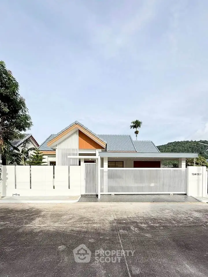 Modern single-story house with white fence and blue roof in a serene neighborhood.