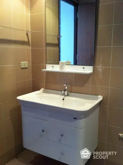 Modern bathroom interior with ceramic sink, wall-mounted mirror, and tiled walls, offering a clean and functional design.