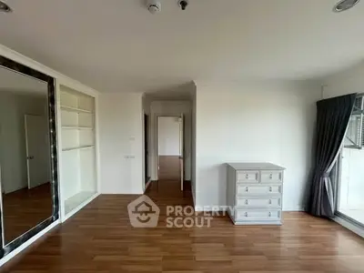 Spacious bedroom with wooden flooring and large mirror, featuring a dresser and built-in shelves.