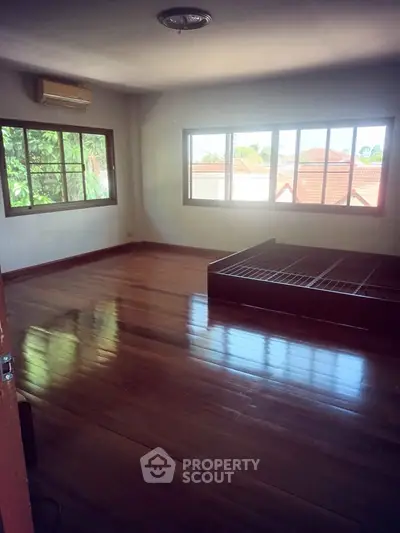 Spacious bedroom with large windows and wooden flooring, offering natural light and serene views.