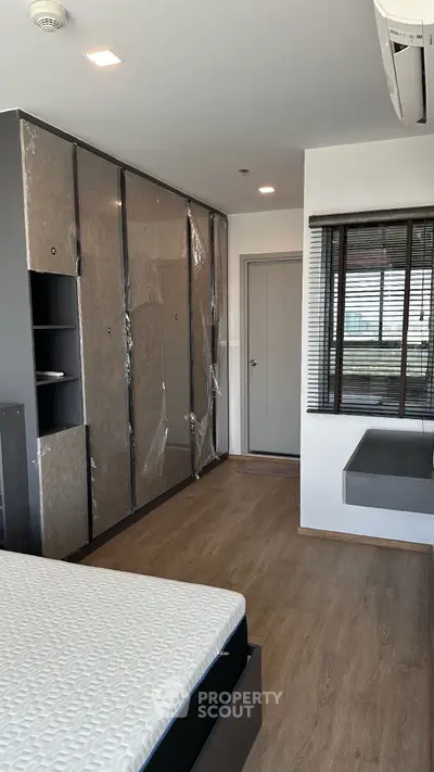 Modern bedroom with sleek wardrobe and large window, featuring minimalist design and hardwood flooring.