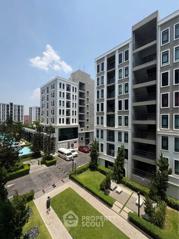 Modern apartment complex with lush garden and pool view under clear blue sky.