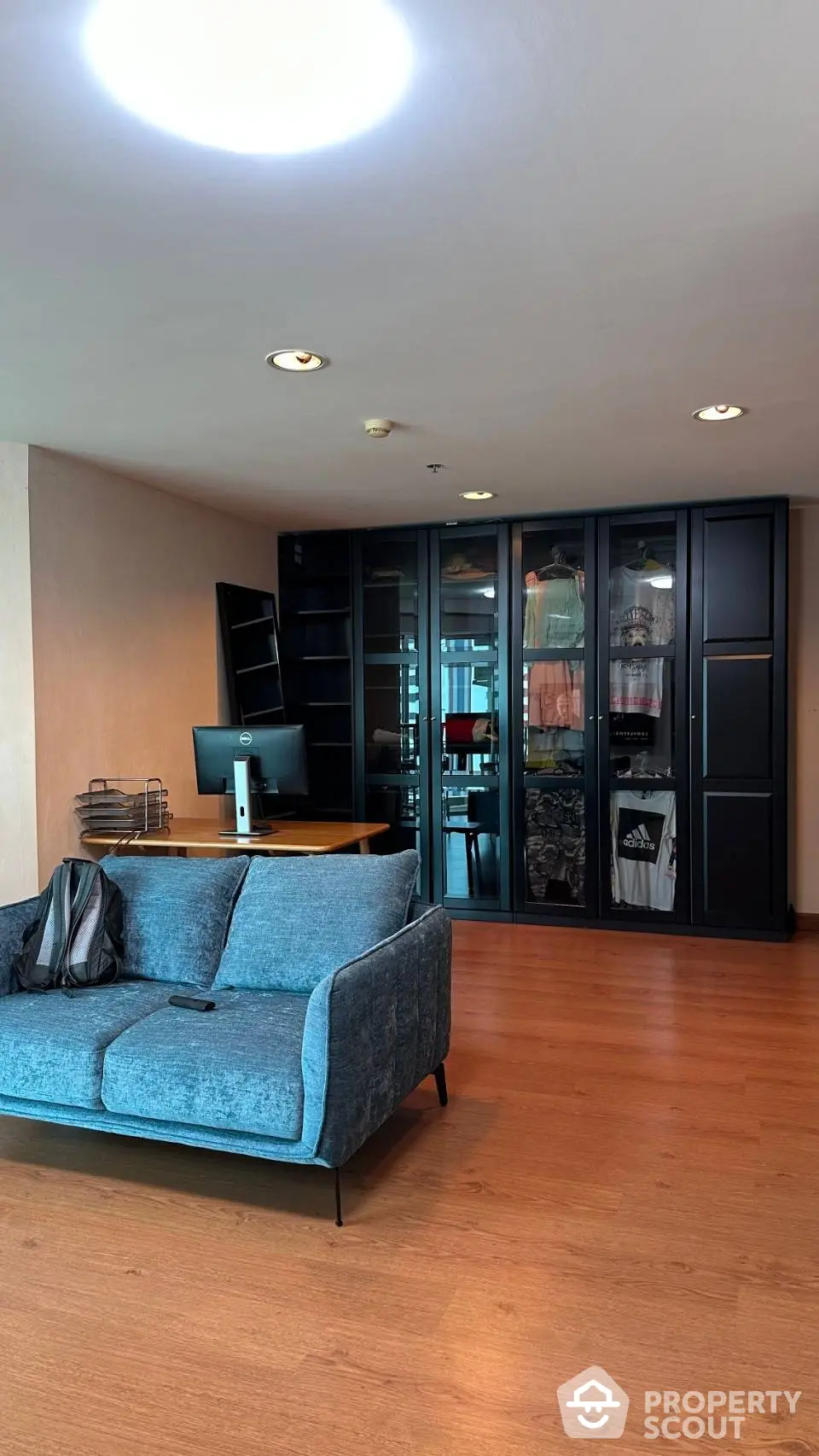 Spacious living room with modern blue sofa, sleek wooden flooring, and ample natural light from the balcony doors, perfect for urban living.