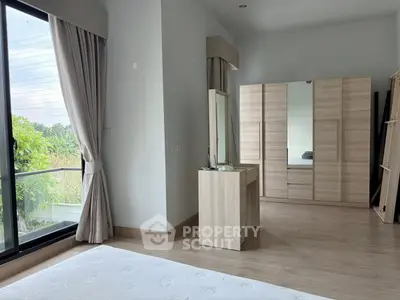Spacious bedroom with large windows and modern wooden furniture, offering a serene view of greenery.