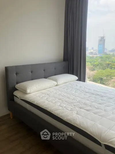 Modern bedroom with large window offering stunning city view and lush greenery.