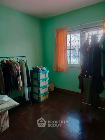 Cozy bedroom with green walls, wooden flooring, and ample natural light from a window.