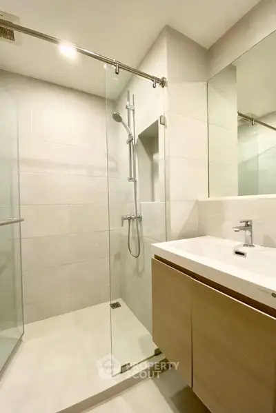 Modern bathroom with glass shower and sleek vanity in contemporary apartment.