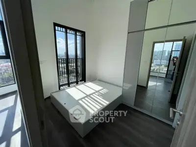Modern bedroom with large windows and city view, featuring sleek flooring and built-in wardrobe.