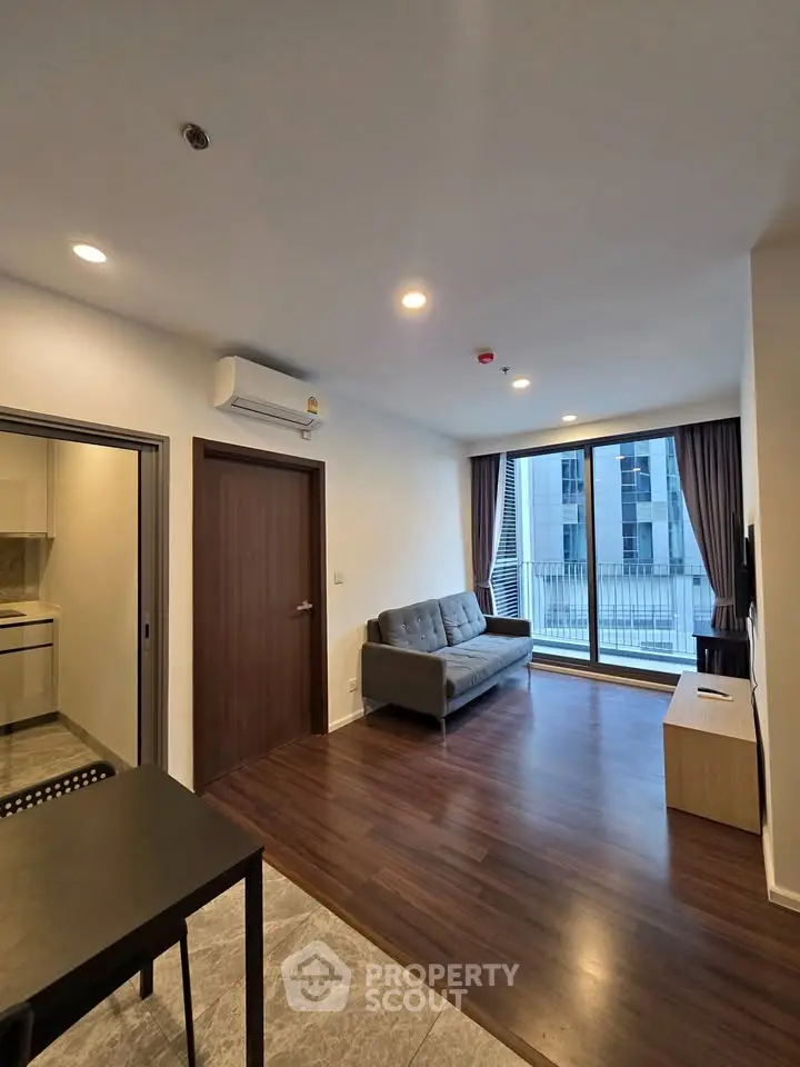 Modern living room with sleek wooden flooring and large windows offering city views.