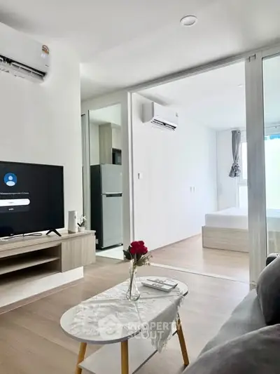 Modern living room with open layout and bedroom view, featuring sleek furniture and natural light.