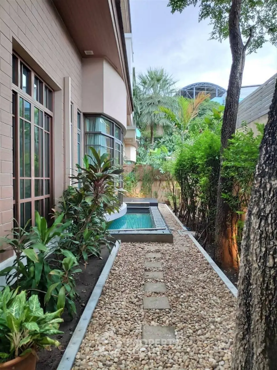 Charming garden pathway leading to a private pool in a serene residential setting.