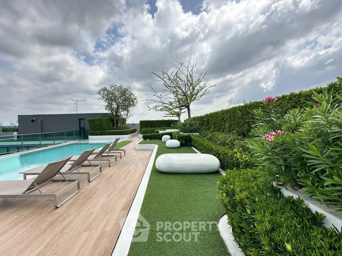 Luxurious rooftop pool area with modern lounge chairs and lush greenery under a cloudy sky.