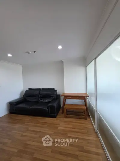 Cozy living room with black leather sofa and wooden table on wooden flooring.
