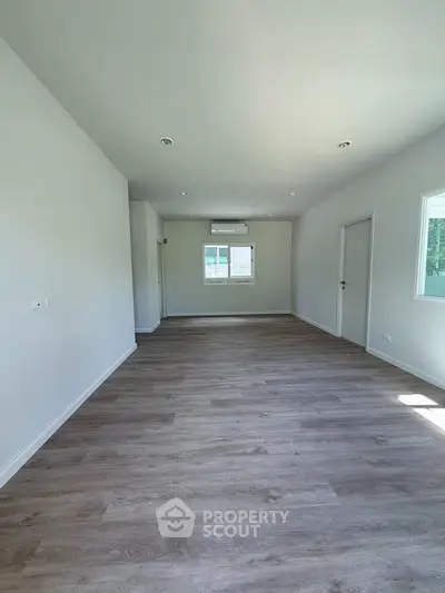 Spacious empty room with wooden flooring and bright natural light, ideal for customization.