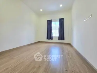 Spacious empty room with wooden flooring and large window, perfect for customization.