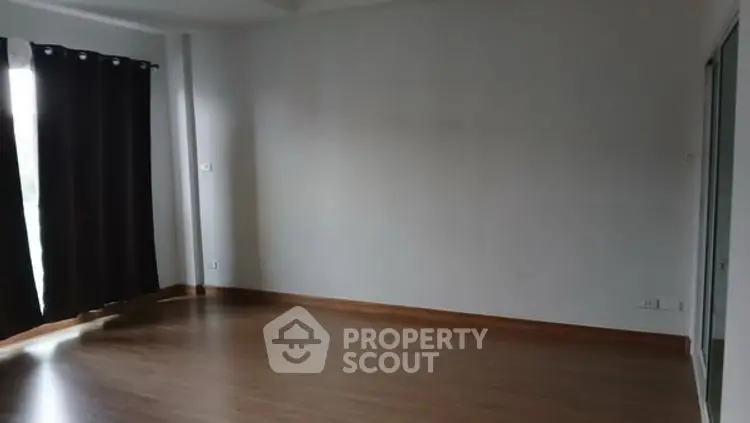 Spacious empty room with wooden flooring and large window, ideal for customization.