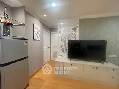 Modern living room with stylish decor and flat-screen TV, featuring a sleek refrigerator and elegant wall art.