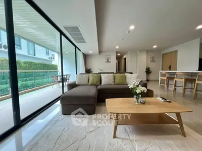 Spacious modern living room with large windows and garden view, featuring a cozy sofa and stylish decor.