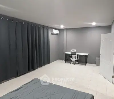Spacious minimalist bedroom with modern desk and chair, featuring dark curtains and air conditioning.
