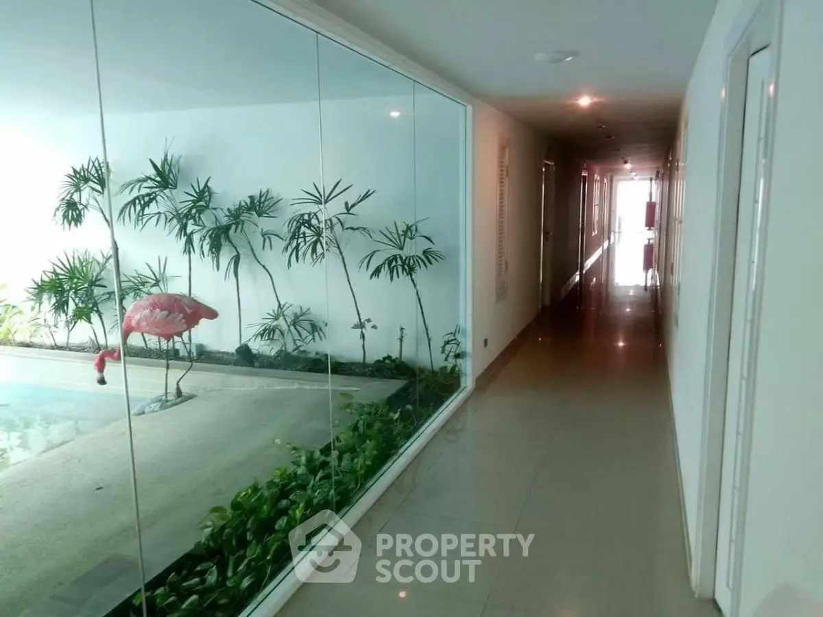Elegant corridor with glass wall overlooking indoor garden and pool area.