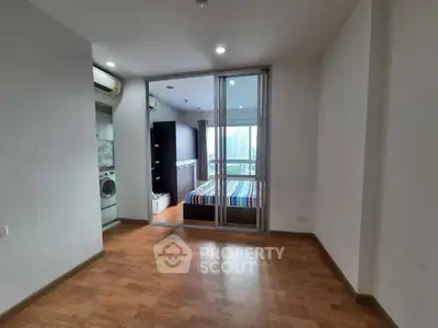Spacious bedroom with wooden flooring and glass sliding doors, featuring a washer and city view.