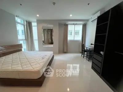 Spacious modern bedroom with large windows and sleek furnishings in a high-rise apartment.