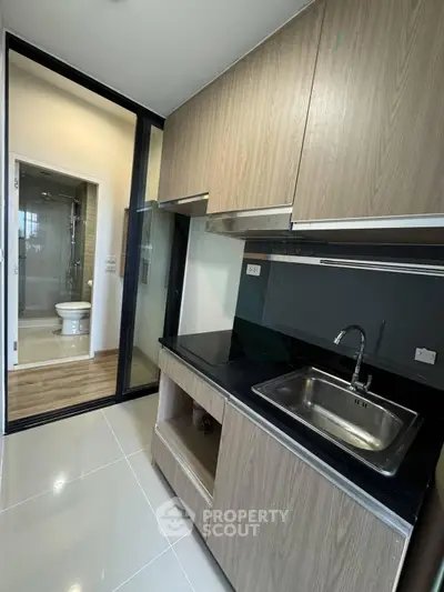 Modern kitchen with sleek cabinetry and black countertop adjacent to a bathroom with glass door.