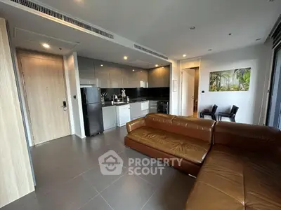 Modern living room with sleek kitchen and leather sofa in open layout apartment.