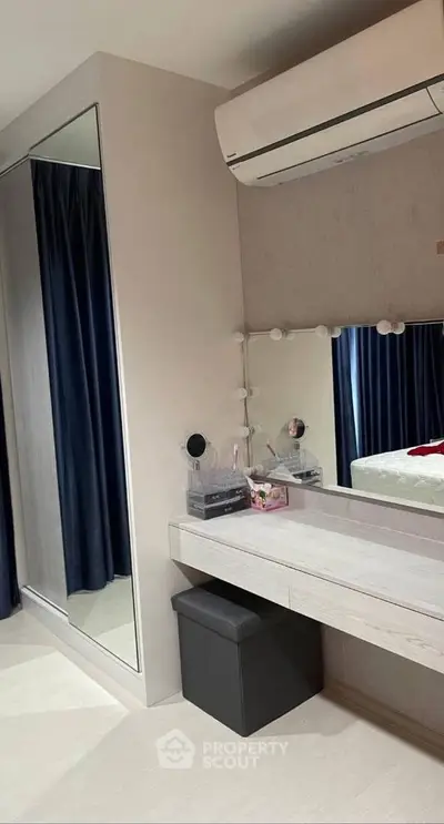 Modern bedroom with sleek vanity and mirrored wardrobe, featuring air conditioning and elegant decor.