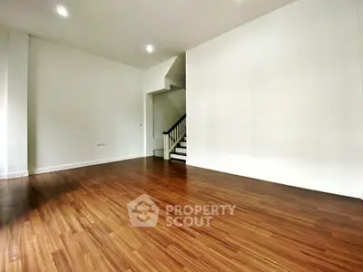 Spacious empty living room with wooden flooring and staircase, perfect for customization.