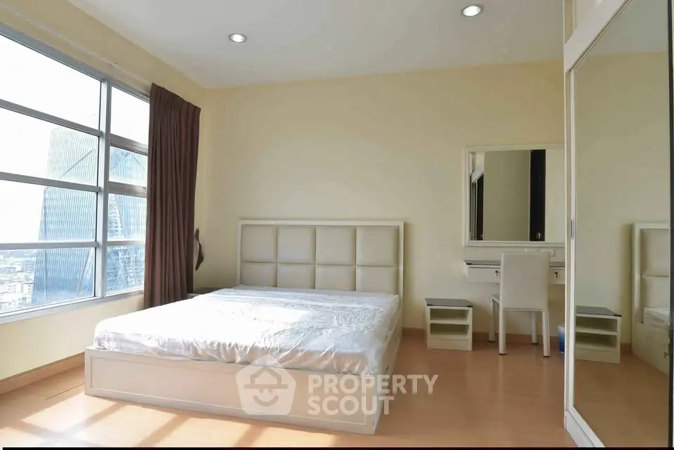 Spacious bedroom with large windows offering stunning city views and modern furnishings.
