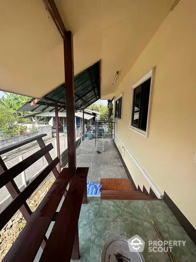 Spacious covered balcony with wooden railing and tiled flooring, offering a peaceful outdoor retreat in a residential home.