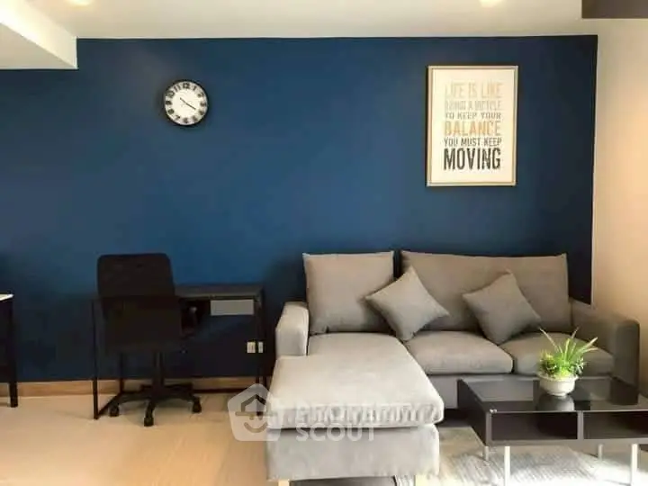 Modern living room with stylish blue accent wall, cozy gray sectional sofa, and sleek black desk.