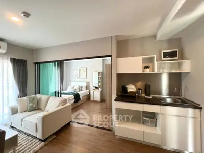Modern open-plan living room with kitchenette and cozy bedroom view.