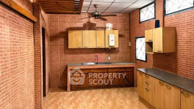 Spacious kitchen with wooden cabinets and brick walls, featuring a ceiling fan and ample natural light.
