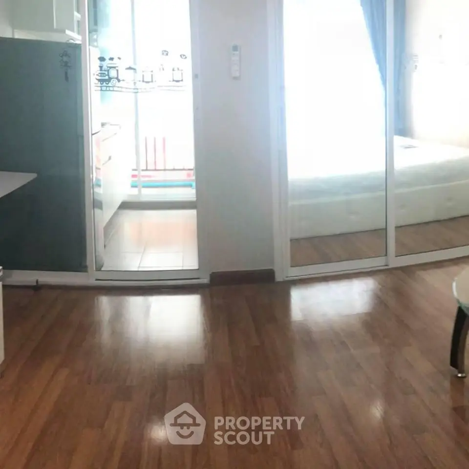 Spacious living area with wooden flooring and glass doors leading to a bright bedroom.
