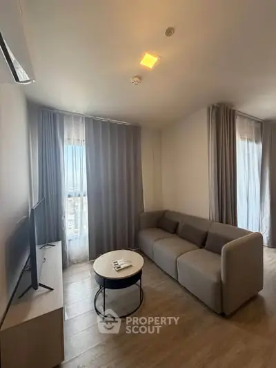 Modern living room with sleek sofa and TV, featuring floor-to-ceiling windows and elegant curtains.