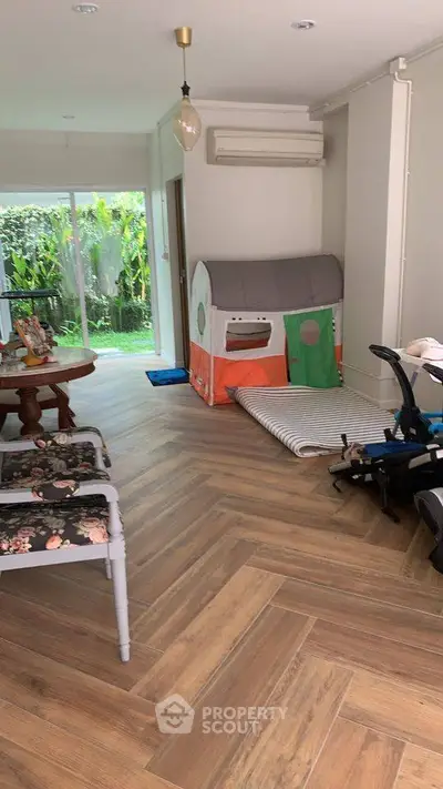 Charming living room with wooden flooring and garden view, featuring a playful kids' tent and cozy seating area.