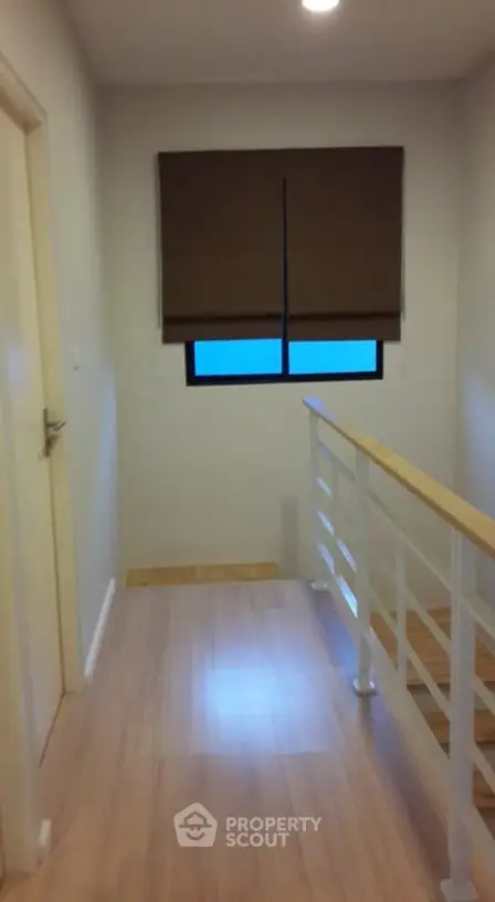 Modern hallway with wooden flooring and railing, featuring a window with brown blinds.