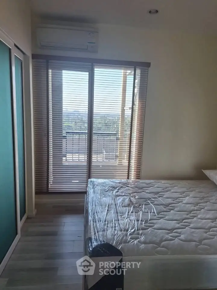 Bright bedroom with large window and balcony access, featuring modern air conditioning and sleek flooring.