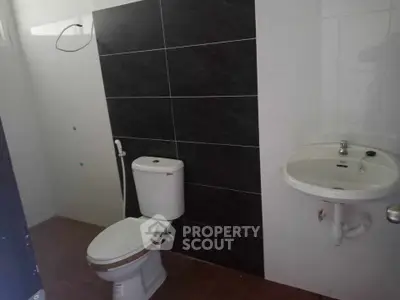 Modern bathroom with sleek black and white tiles, featuring a toilet and wall-mounted sink.