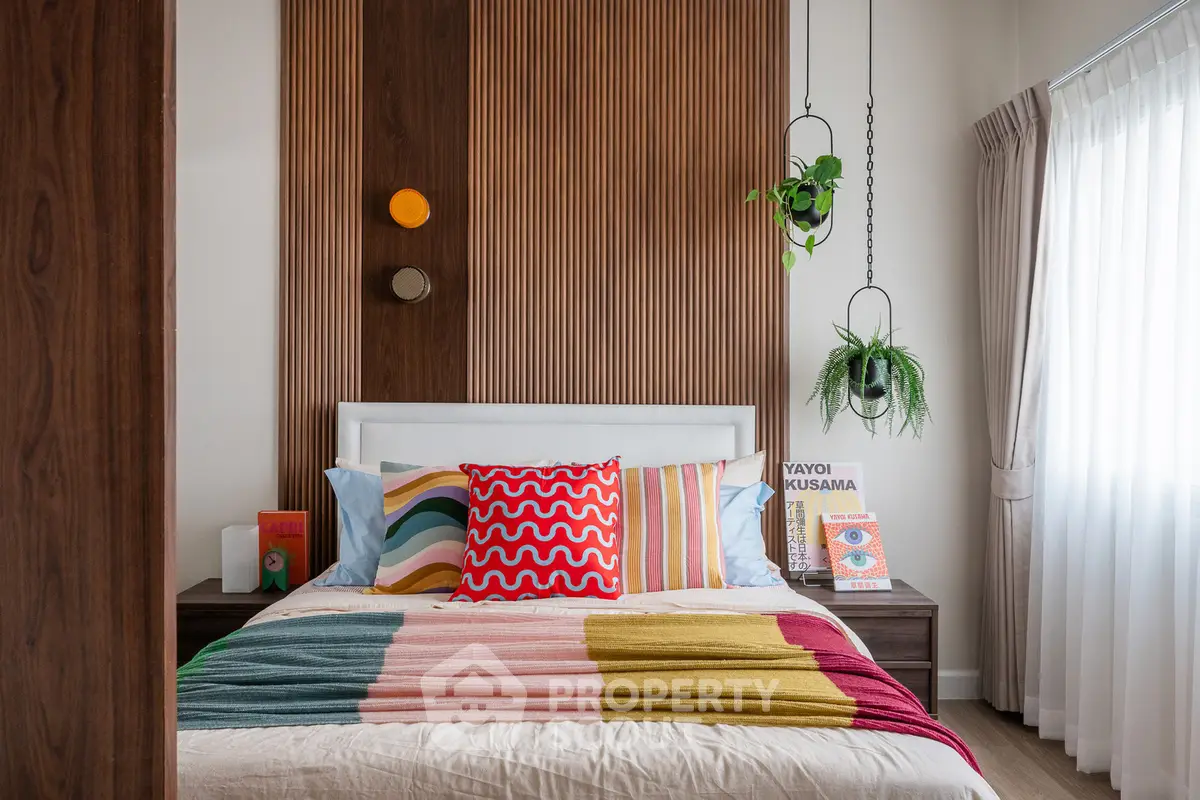 Stylish bedroom with colorful bedding and modern decor, featuring wooden accent wall and hanging plants.