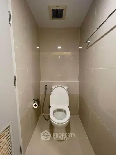 Modern bathroom with sleek design and neutral tones featuring a toilet and bidet spray.